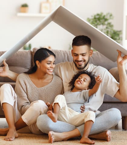 a man and woman sitting on the floor with their daughter holding a roof over their