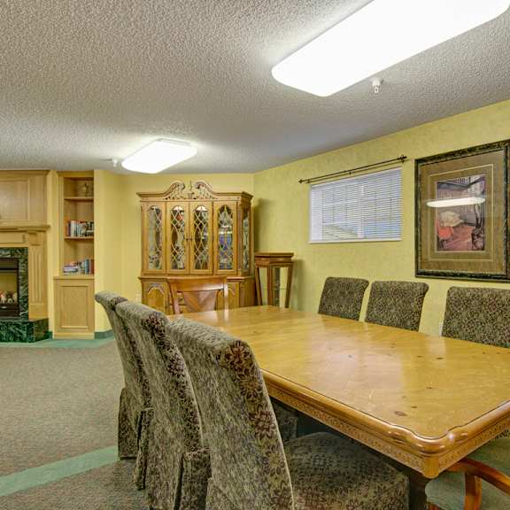 A common room with a dining table and chair with a fireplace in the background at Heritage Park. 