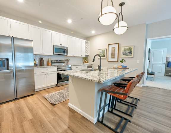 A kitchen with a refrigerator, microwave, and bar stools.
