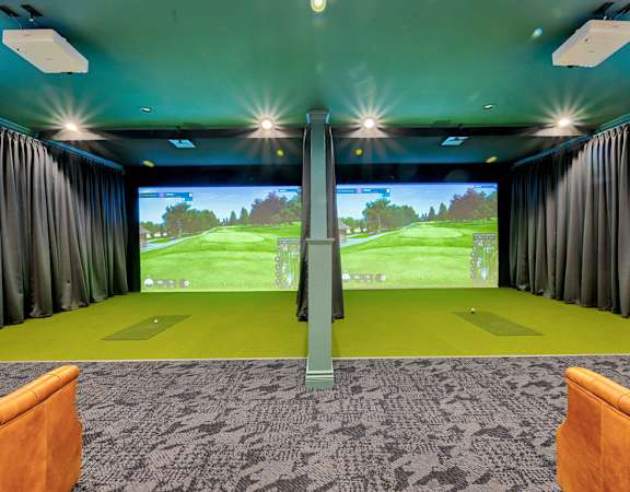 A room with a golf simulator and two chairs.