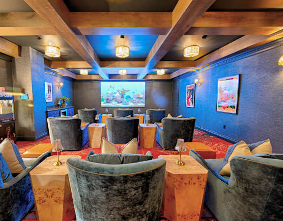 A row of plush chairs are arranged in a room with a blue wall and a television screen.