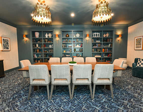 A room with a long table and chairs and a bookshelf in the background.