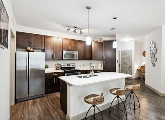 a kitchen with a large white island with three stools in front of it at The Loree Apartments, Jacksonville, FL