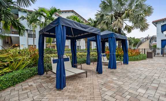 a seating area with blue curtains and chairs on a brick patio at Barcelona Jupiter, Jupiter, FL