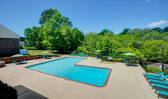 a swimming pool with chairs and umbrellas and trees in the background