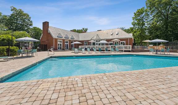 A large outdoor swimming pool with a brick patio and a house in the background.