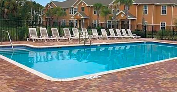 a large pool with white chairs in front of an apartment building