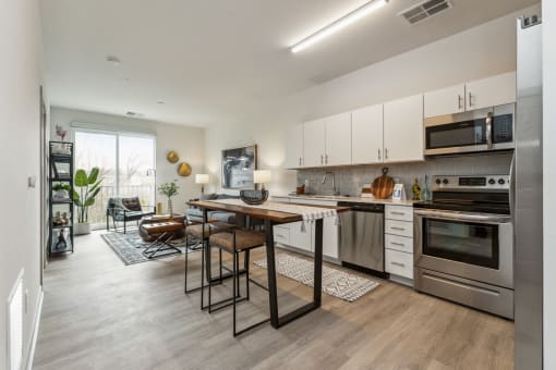 a kitchen with white cabinets and stainless steel appliances and a wooden table with two chairs At Rocketts Landing Apartments, PRG Real Estate, Richmond, Virginia