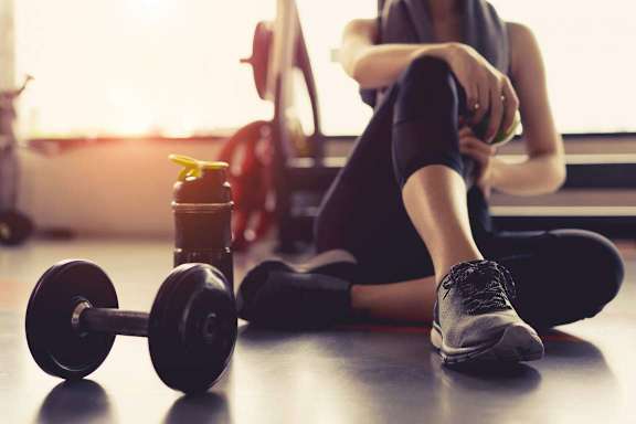 A woman is sitting on the floor with a dumbbell and a water bottle next to her.