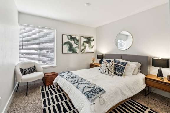 A bedroom with a bed, chair, and two paintings on the wall.