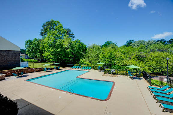 a swimming pool with chairs and umbrellas and trees in the background at Lakecrest Apartments, PRG Real Estate Management, Greenville, South Carolina