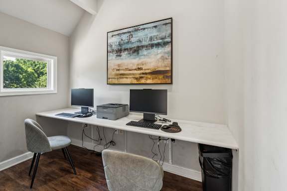A room with a desk, two chairs, and a painting on the wall.