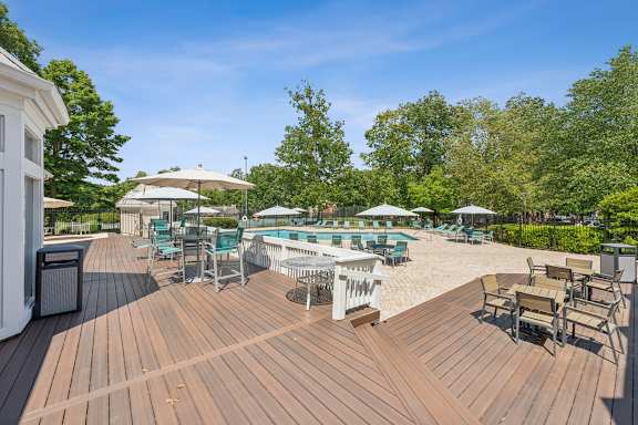 A wooden deck with chairs and umbrellas overlooking a pool.