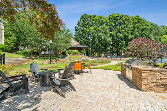 A patio with chairs and a table is surrounded by trees. at Woodcreek Apartments, North Carolina