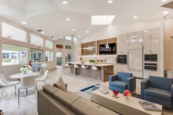 A modern living room with a kitchen in the background at The Villages Apartment of Bayan Grove in Boynton Beach, FL
