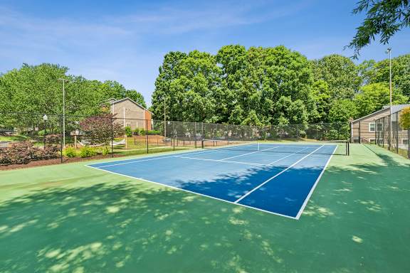 A tennis court surrounded by trees and a fence. at Woodcreek Apartments, North Carolina