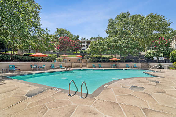 A swimming pool surrounded by trees and chairs.