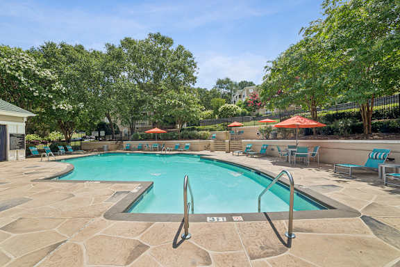 A pool surrounded by trees and chairs.