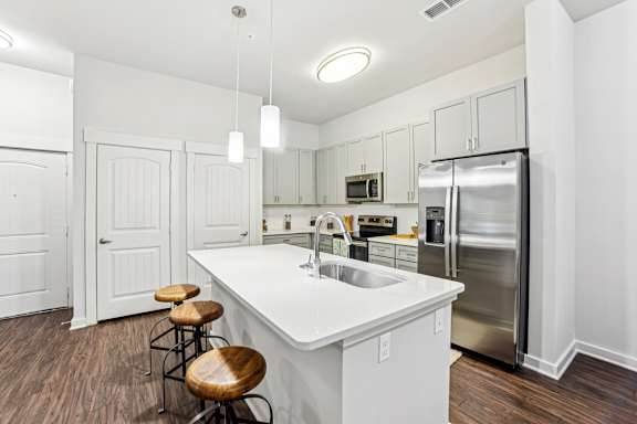 A white kitchen with a refrigerator, sink, and bar stools.