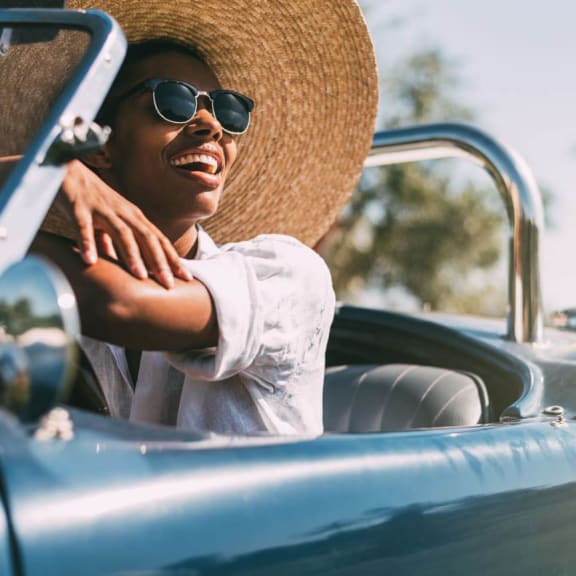 a woman driving a convertible car with a hat on her head