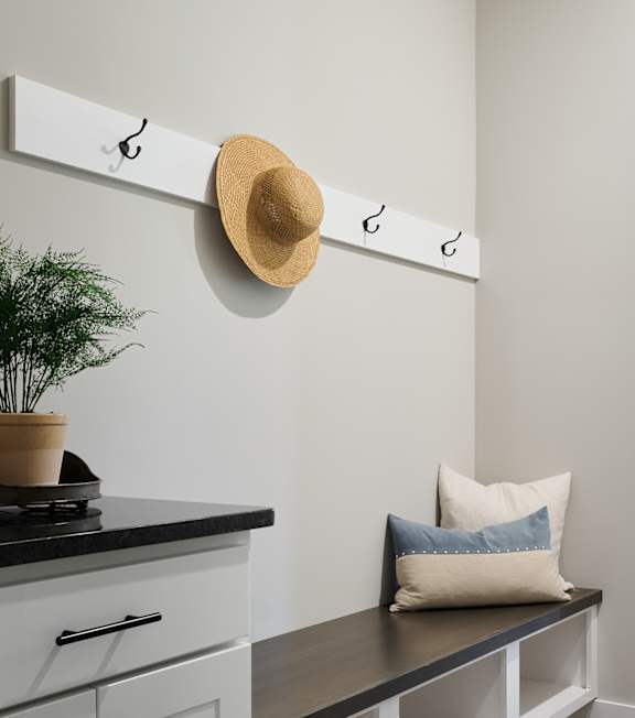 A kitchen with a bench and a hat hanging on a hook.