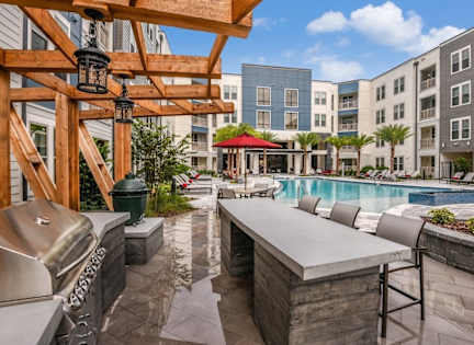 A pool area with a bar and chairs is surrounded by apartment buildings. at CODA Apartments , Orlando, FL, 32826