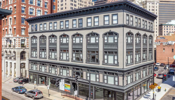 A large, old building with many windows is in the middle of a city street.