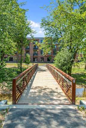 A wooden footbridge over a running creek with large trees at Keva Flats Apartments in Exton, PA