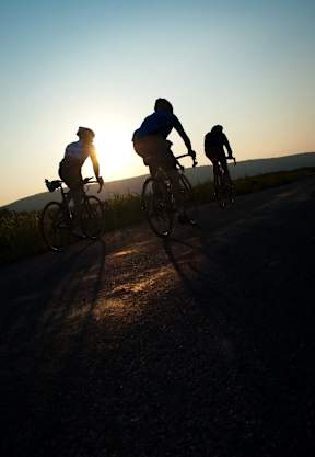 Three cyclists riding on a road during sunset.
