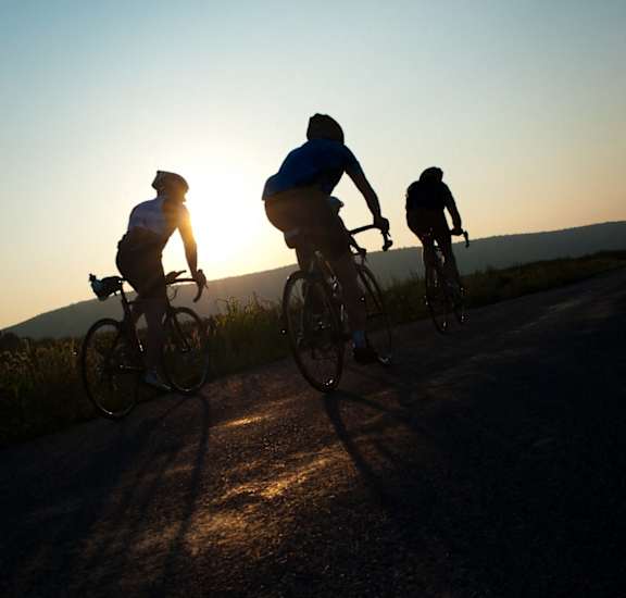 Three cyclists riding on a road during sunset.