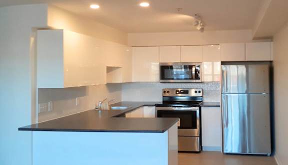 A modern kitchen with a stainless steel refrigerator and wooden flooring.