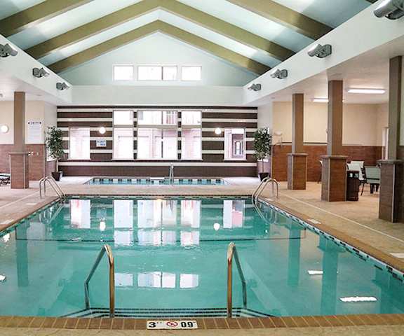 Resident Pool with Lounging and seating areas The indoor pool with tables, chairs, and pool chairs surrounded by white and brown walls with large windows at Renaissance Heights Apartment Homes.