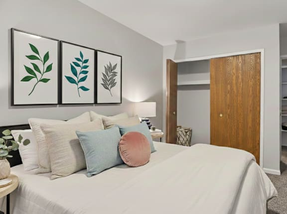 A bedroom with a bed, pillows, a lamp, and a painting of leaves on the wall.