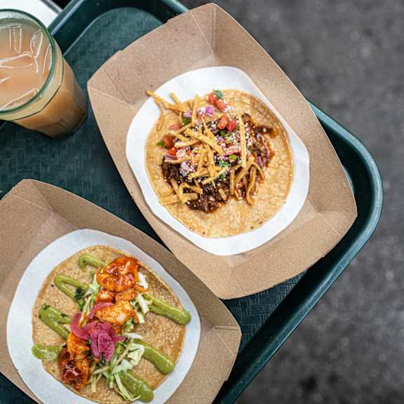 two tacos in a box on a table with a cup of coffee