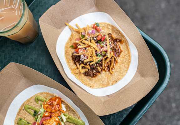 two tacos in a box on a table with a cup of coffee