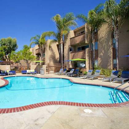 A large outdoor swimming pool surrounded by palm trees and lounge chairs.at Pacific Bay Club Apartments, San Diego, 92117