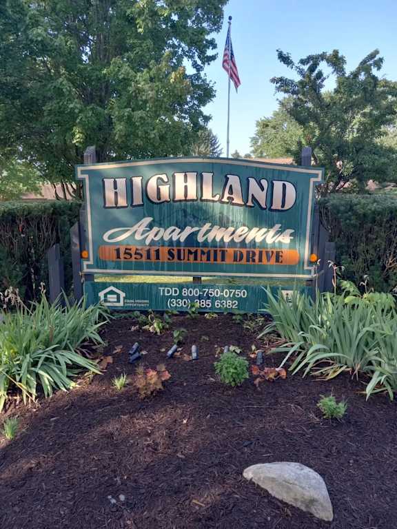 A sign for Highland Apartments is displayed in front of some trees.
