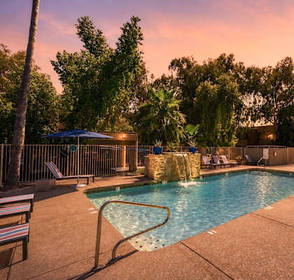 A pool surrounded by trees and chairs with a sunset in the background.