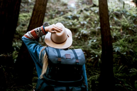 a woman with a backpack and a hat in the woods