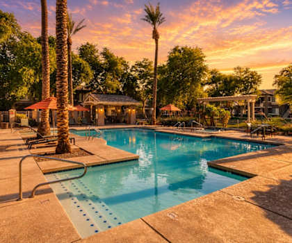 A pool surrounded by palm trees and a sunset sky.