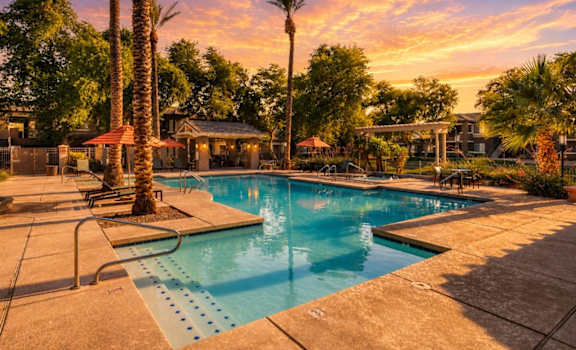 A pool surrounded by palm trees and a sunset sky.