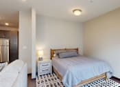 Thumbnail 3 of 11 - the bedroom area in a studio apartment with bed and bedside table with lamp
