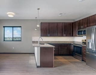This 2 bedroom Snowdrop with den floor plan at WH Flats features an open kitchen with dark cabinets, granite countertops, and large peninsula.
