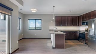This 2 bedroom Snowdrop with den floor plan at WH Flats features an open kitchen with dark cabinets, granite countertops, and large peninsula.