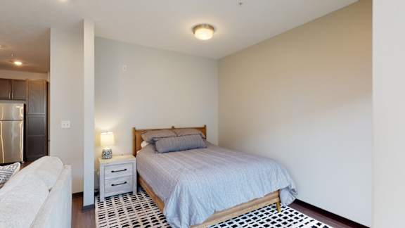 the bedroom area in a studio apartment with bed and bedside table with lamp