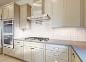 Thumbnail 2 of 13 - A gourmet kitchen with a stainless steel range hood over a 5-burner gas stovetop, a pot filler faucet, two stainless steel ovens, and taupe cabinets.