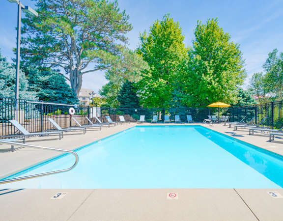 Swimming pool with lounge chairs for sunbathing and table shaded by yellow umbrella in the back