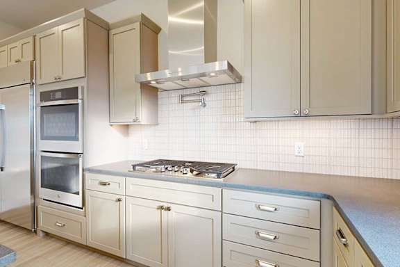 A gourmet kitchen with a stainless steel range hood over a 5-burner gas stovetop, a pot filler faucet, two stainless steel ovens, and taupe cabinets.