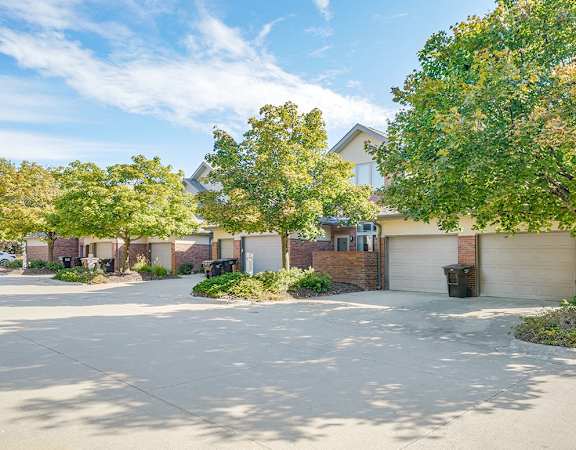 the exteriors of a row of villas with attached garages and trees lining the road