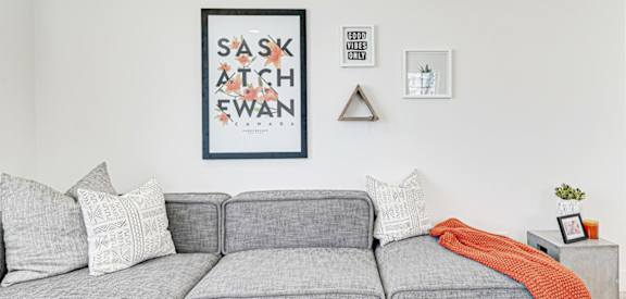 A grey couch with a red throw and a framed poster reading "Saskatchewan" on the wall behind it.